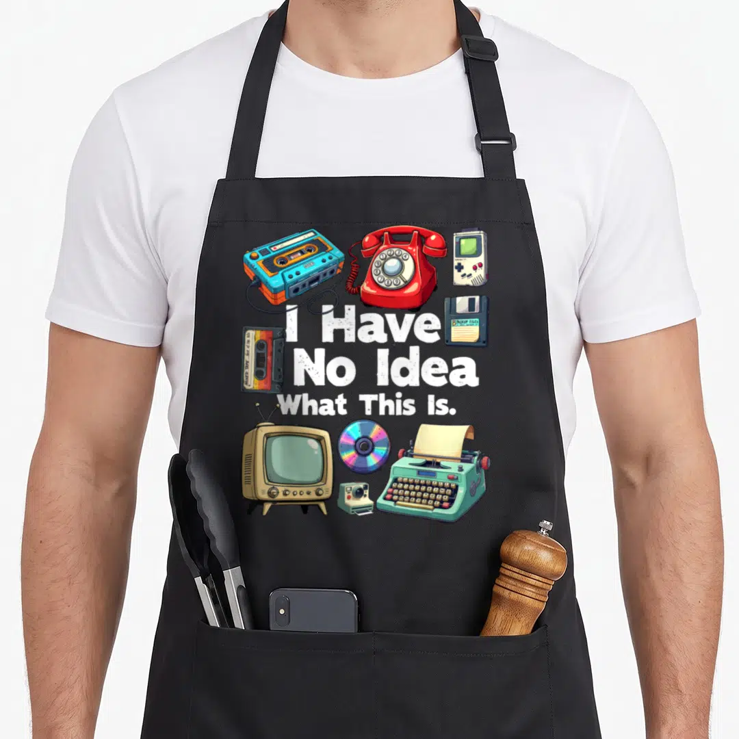 Funny bro 80s apron - I Have No Idea What This Is text surrounded by retro cassette, phone, tv, and typewriter — shown on a black cotton canvas apron against a white background