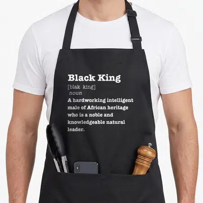 King african print apron - White stacked typography defining Black King as a noble African leader — shown on a black cotton canvas apron against a white background