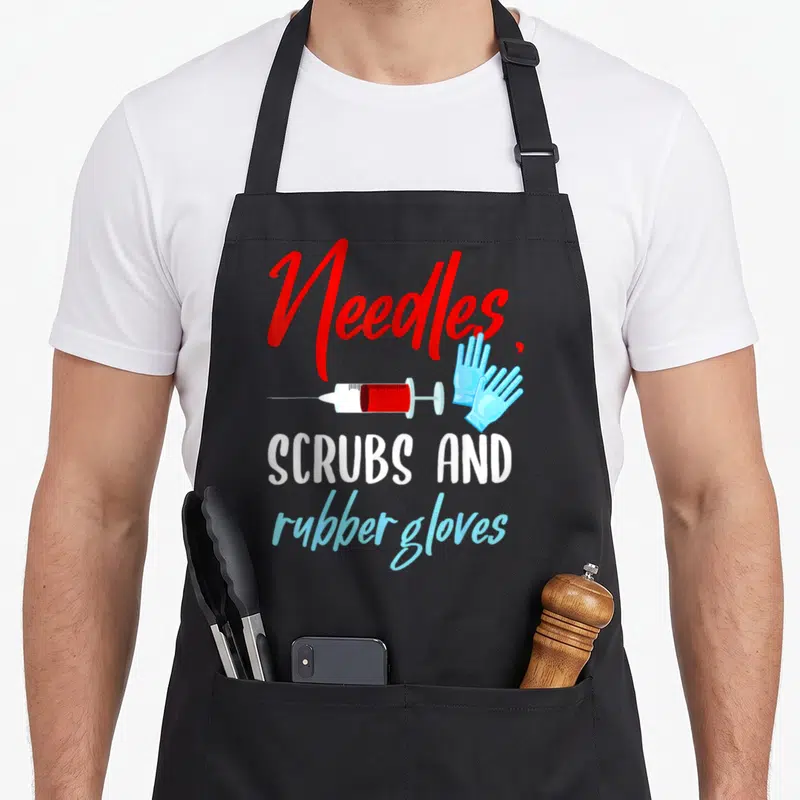 Needle nurse apron - Red Needles text with syringe and blue gloves above white and blue scrub text — shown on a black cotton canvas apron against a white background