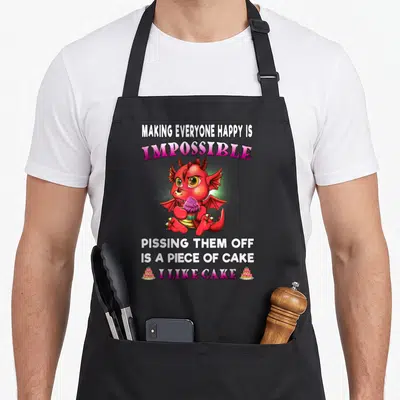 Dragon making an apron - Red cartoon dragon holding pink cupcake with sarcastic quote about cake and annoyance — shown on a black cotton canvas apron against a white background