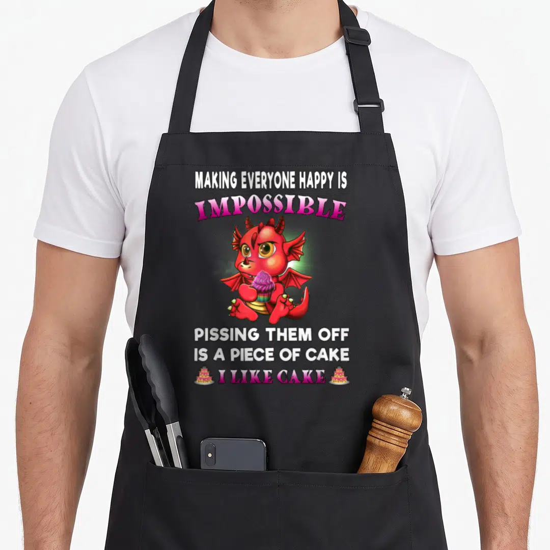 Dragon making an apron - Red cartoon dragon holding pink cupcake with sarcastic quote about cake and annoyance — shown on a black cotton canvas apron against a white background