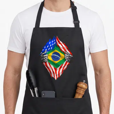 Brazil brazilian american flag apron - Hands tearing USA flag to reveal Brazil flag with ORDEM E PROGRESSO text — shown on a black cotton canvas apron against a white background