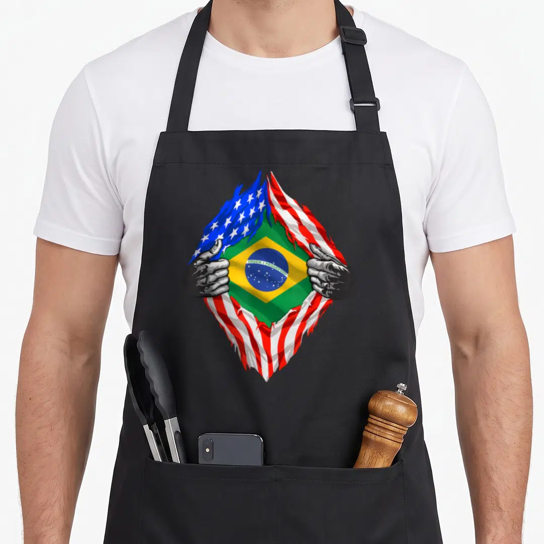 Brazil brazilian american flag apron - Hands tearing USA flag to reveal Brazil flag with ORDEM E PROGRESSO text — shown on a black cotton canvas apron against a white background