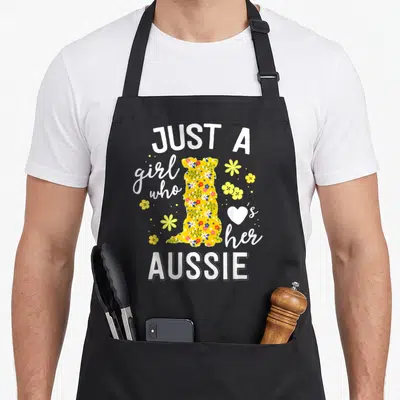 Floral australian apron - Flower-filled dog silhouette with JUST A girl who her AUSSIE text and heart — shown on a black cotton canvas apron against a white background