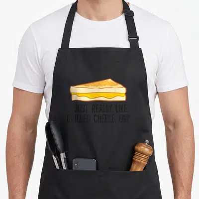 Cute cheese grilled apron - Cartoon grilled cheese sandwich above text I just really like grilled cheese ok — shown on a black cotton canvas apron against a white background