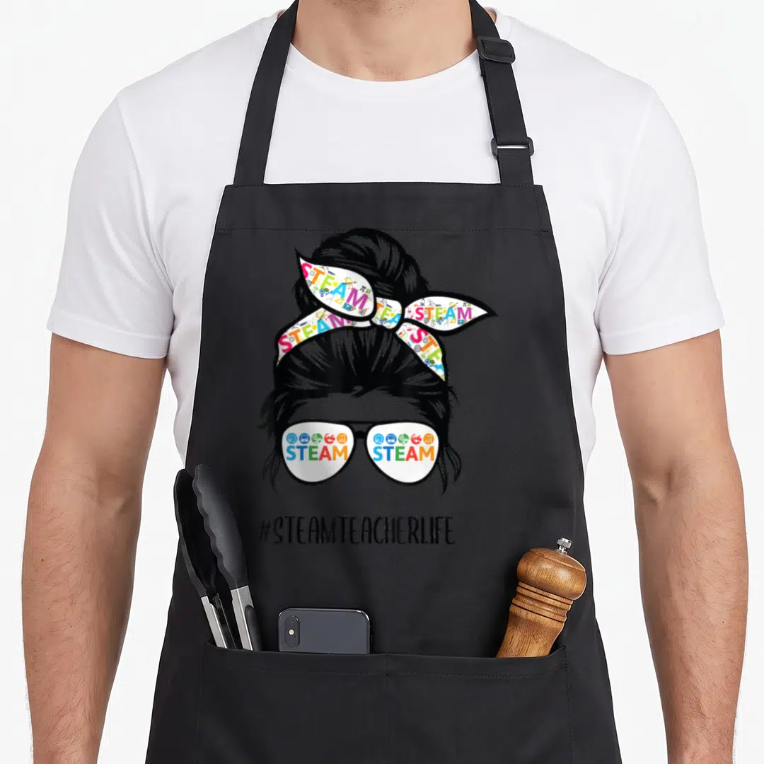Steam messy aprons - Woman silhouette with STEAM text in glasses and headband, #STEAMTEACHERLIFE hashtag below — shown on a black cotton canvas apron against a white background