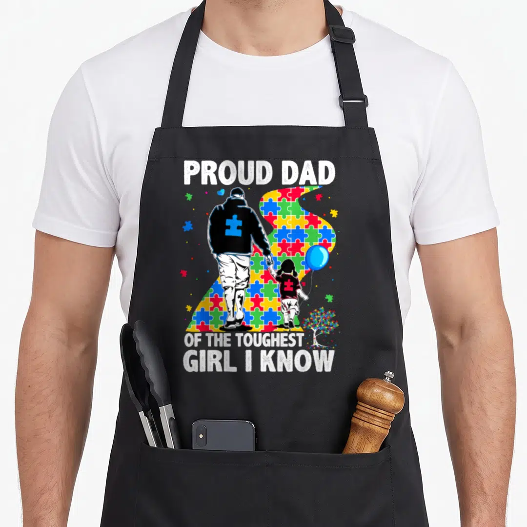 Proud autism awareness apron - Father and daughter silhouette walking on colorful puzzle pieces with blue balloon — shown on a black cotton canvas apron against a white background