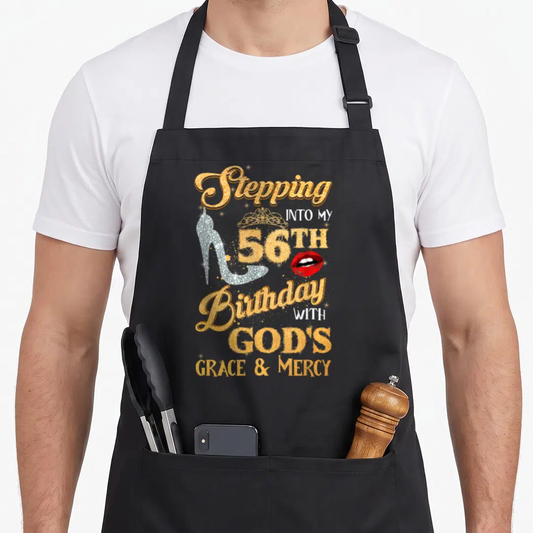 Step grace apron - Gold 56th birthday text with silver heel, crown, and red lips on black apron — shown on a black cotton canvas apron against a white background
