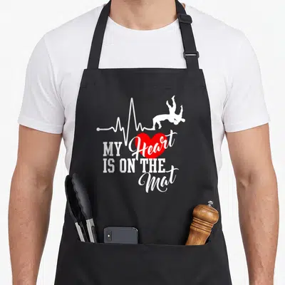 Mat wrestling apron - White heartbeat line with wrestler silhouettes and red heart above stacked text — shown on a black cotton canvas apron against a white background