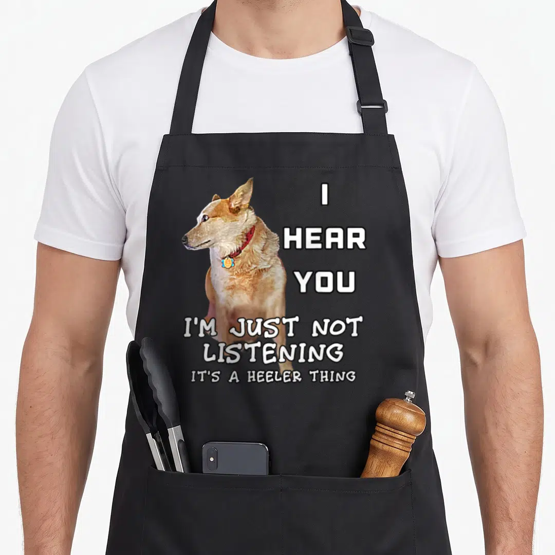 Heeler owner dog apron - Photo of tan dog with red collar next to white text reading I hear you I'm just not listening — shown on a black cotton canvas apron against a white background