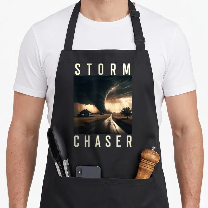 Storm chaser meteorologist apron - Tornado landscape photo between STORM and CHASER text in grey and brown — shown on a black cotton canvas apron against a white background