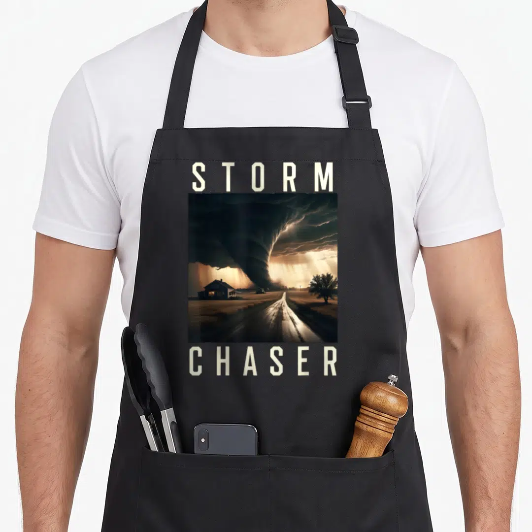 Storm chaser meteorologist apron - Tornado landscape photo between STORM and CHASER text in grey and brown — shown on a black cotton canvas apron against a white background