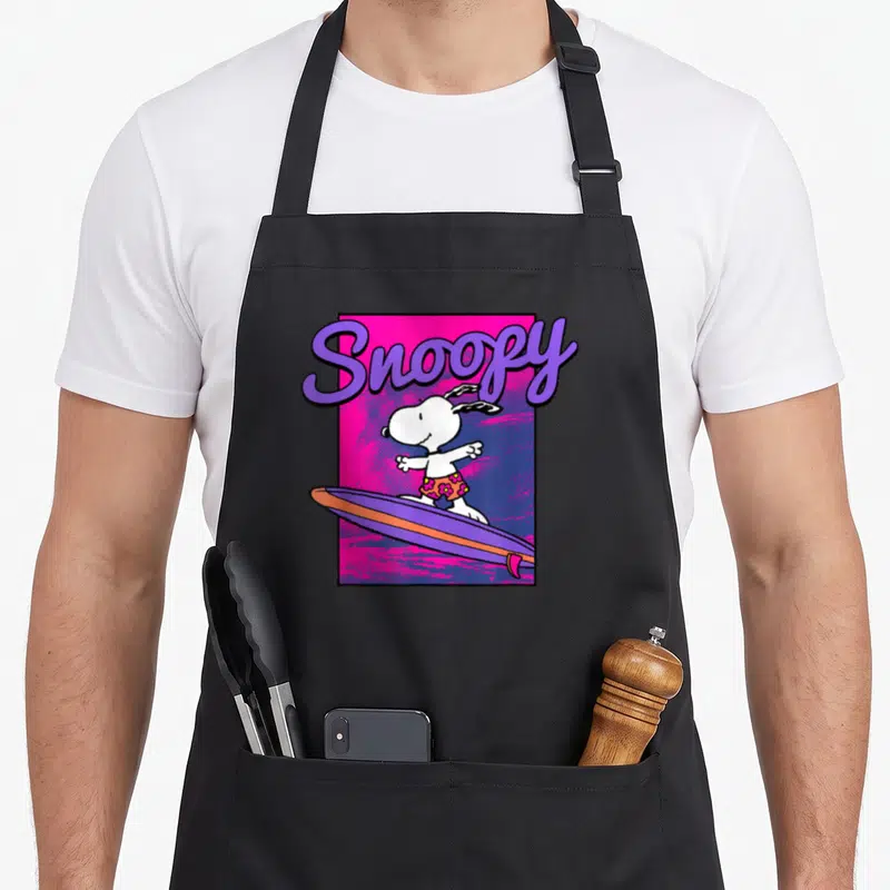 Neon surfing apron - Snoopy surfing on purple board with pink background and purple script text — shown on a black cotton canvas apron against a white background