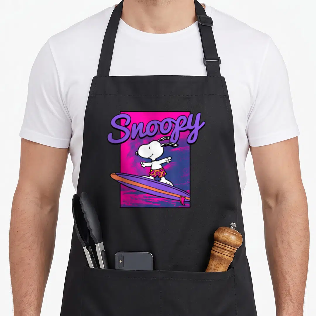 Neon surfing apron - Snoopy surfing on purple board with pink background and purple script text — shown on a black cotton canvas apron against a white background