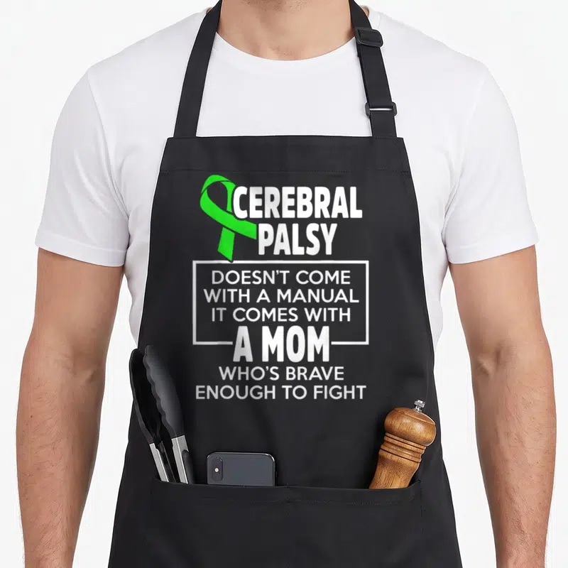 Warrior survivor cerebral palsy awareness apron - Green ribbon and white text reading Cerebral Palsy doesn't come — shown on a black cotton canvas apron against a white background