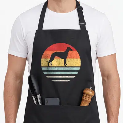 Whippet mother's apron - Grey dog silhouette on red orange yellow teal striped circle — shown on a black cotton canvas apron against a white background