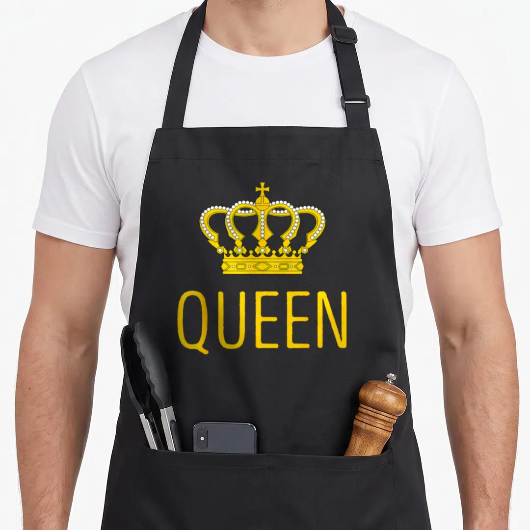 Cute birthday queen of baking apron - Yellow crown with white pearls above QUEEN text in bold font — shown on a black cotton canvas apron against a white background