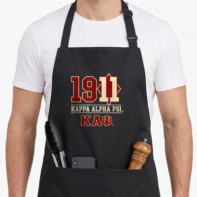 Cool psi alpha apron - 1911 KAPPA ALPHA PSI text and ΚΑΨ Greek letters in crimson and cream stacked vertically — shown on a black cotton canvas apron against a white background