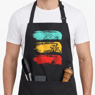 Triathlon biker apron - Three distressed paint strokes in teal, yellow, and red containing grey silhouettes — shown on a black cotton canvas apron against a white background