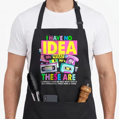 80s 90s theme chef outfit with apron - I HAVE NO IDEA 80s WHAT 90's THESE ARE text with cassette and roller skate — shown on a black cotton canvas apron against a white background