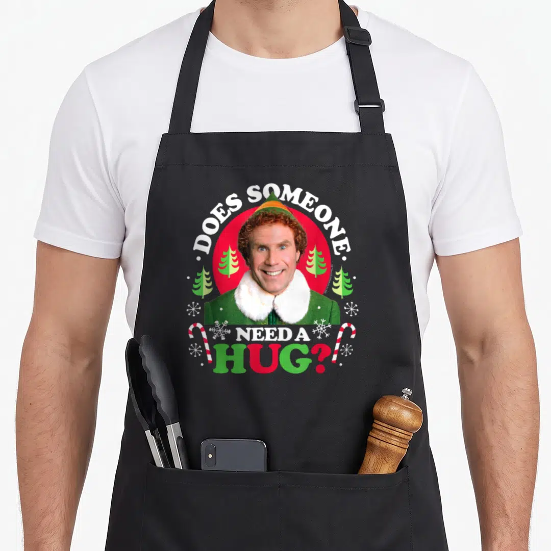Doe christmas elf apron - Buddy the Elf photo with text DOES SOMEONE NEED A HUG and candy canes — shown on a black cotton canvas apron against a white background