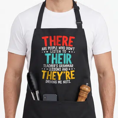 Nazy english apron - Stacked text reading there are people who didn't listen to their teacher's grammar lessons — shown on a black cotton canvas apron against a white background