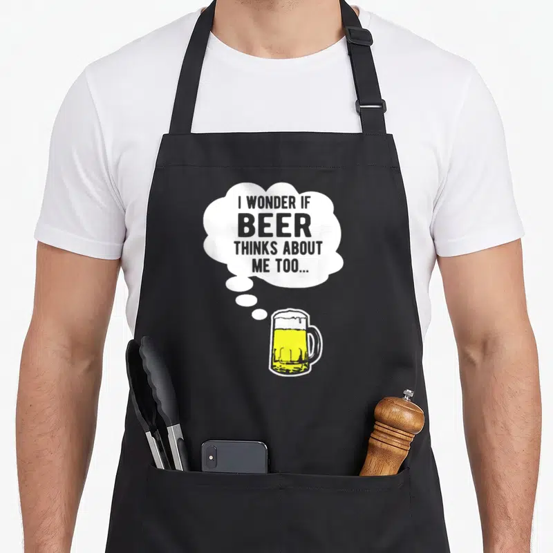 Retro wonder beer apron - Cartoon beer mug with thought bubble reading I wonder if beer thinks about me too — shown on a black cotton canvas apron against a white background