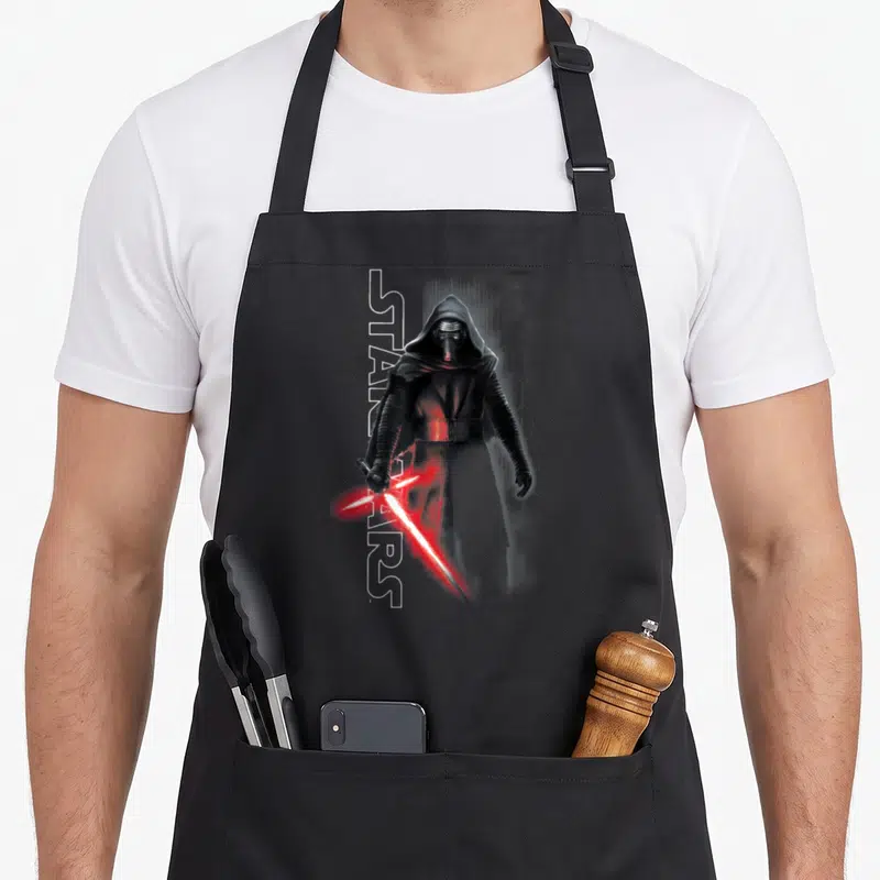 Episode x apron - Kylo Ren with red lightsaber overlapping vertical STAR WARS text in black and white — shown on a black cotton canvas apron against a white background