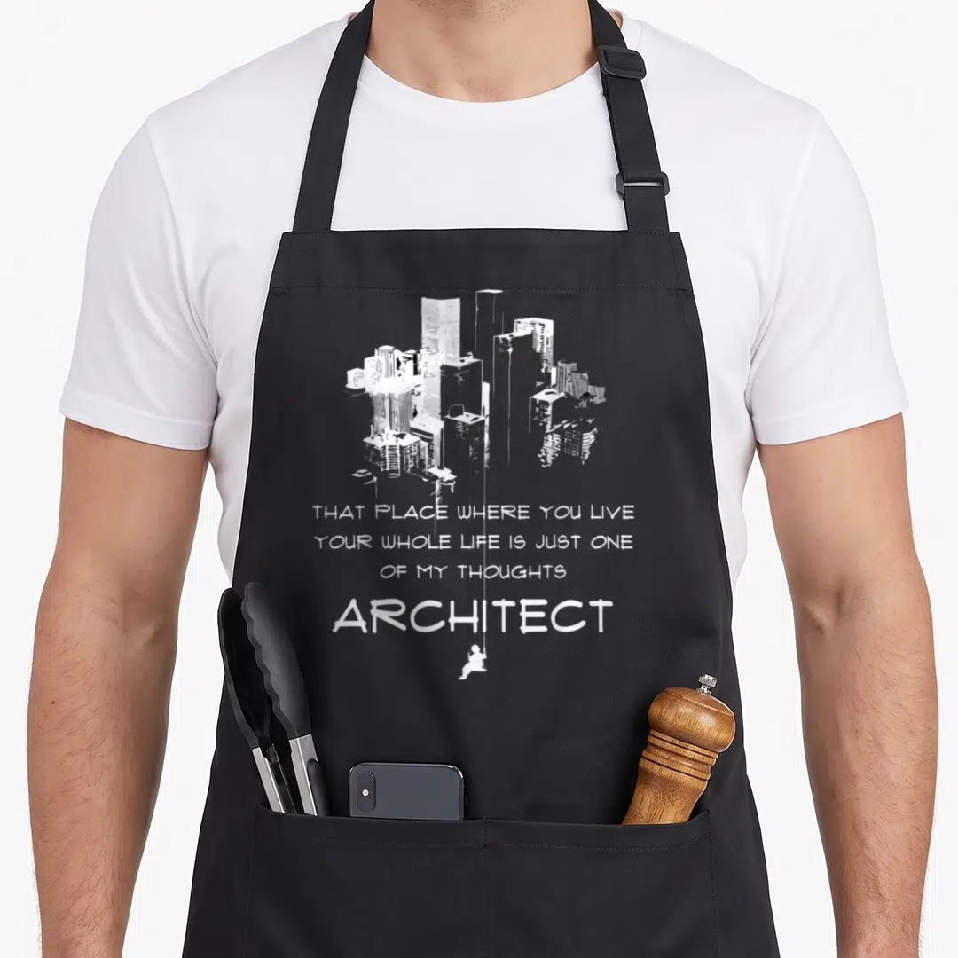 Architecture definition architect apron - Grey minimalist cityscape with white stacked text and a tiny figure hanging — shown on a black cotton canvas apron against a white background