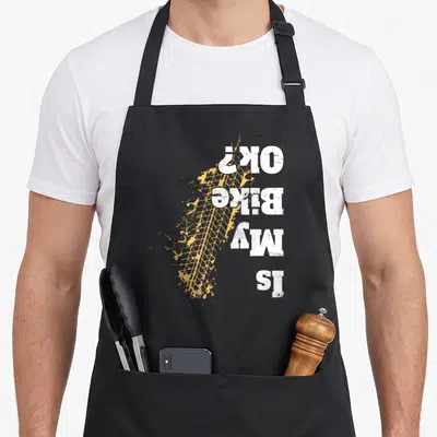 Offroad biker apron - Vertical Is My Bike Ok text over yellow distressed tire track and splatter — shown on a black cotton canvas apron against a white background