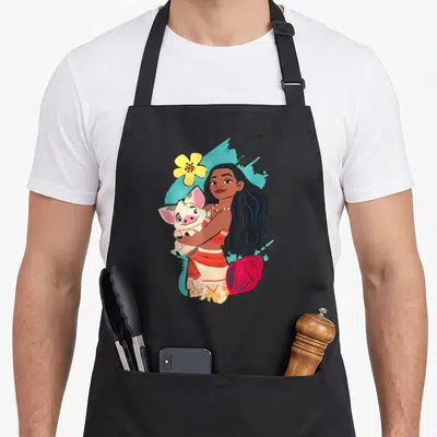 Pua princess apron - Moana holding a pig with yellow flower and red shell on blue background — shown on a black cotton canvas apron against a white background