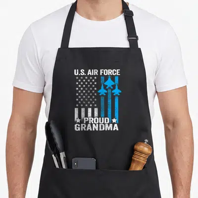 Usaf grandma apron - Distressed US Air Force flag with three blue jets and Proud Grandma text flanked by stars — shown on a black cotton canvas apron against a white background
