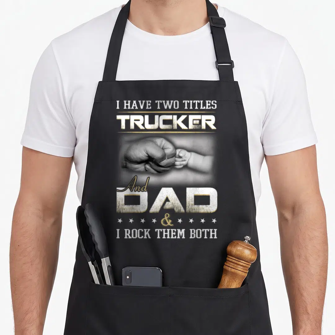 Driver trucking truck apron - Fist bump between adult and baby hands with Trucker Dad quote in white beige grey — shown on a black cotton canvas apron against a white background