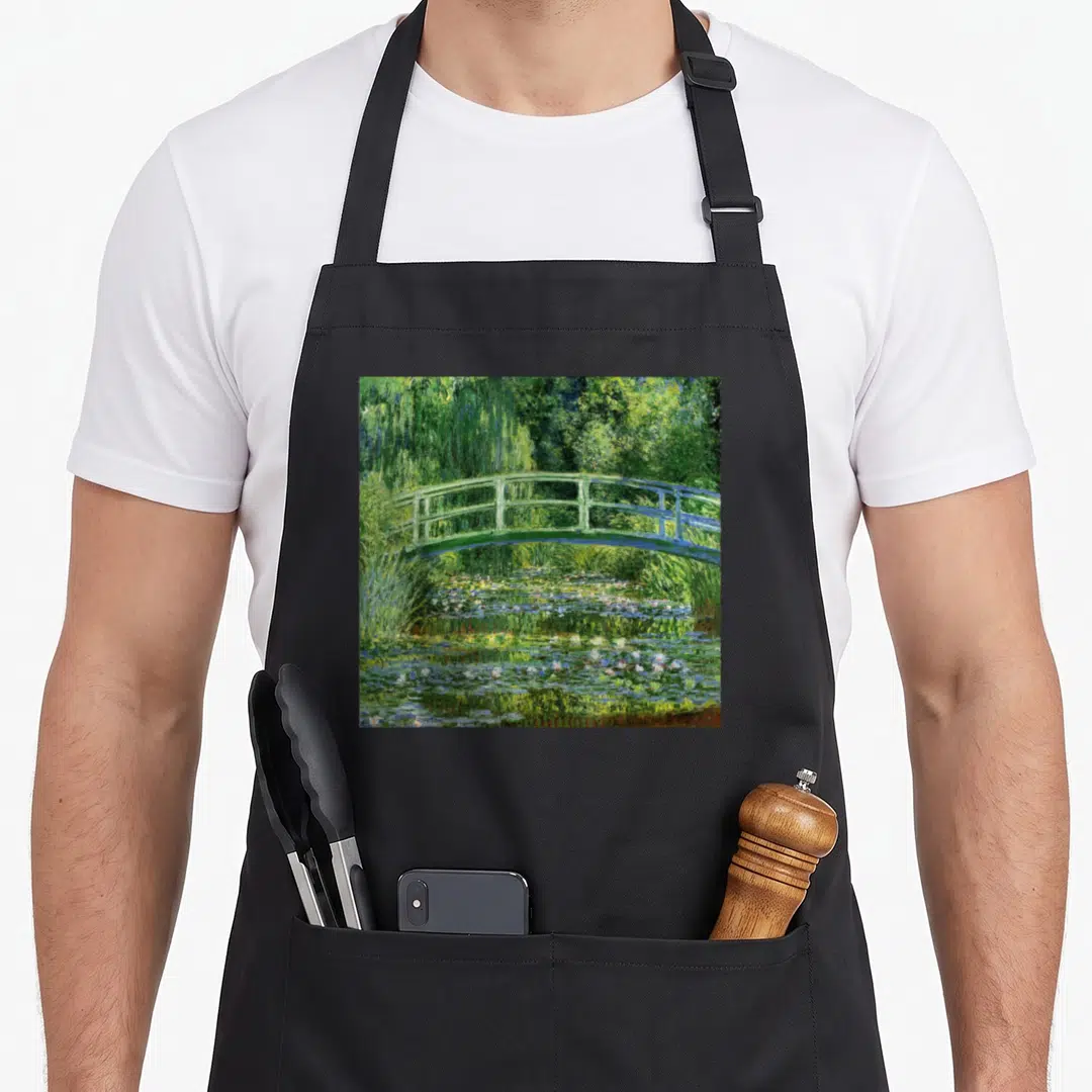 Water white lily apron - Green arched bridge over a pond with water lilies in a watercolor style — shown on a black cotton canvas apron against a white background