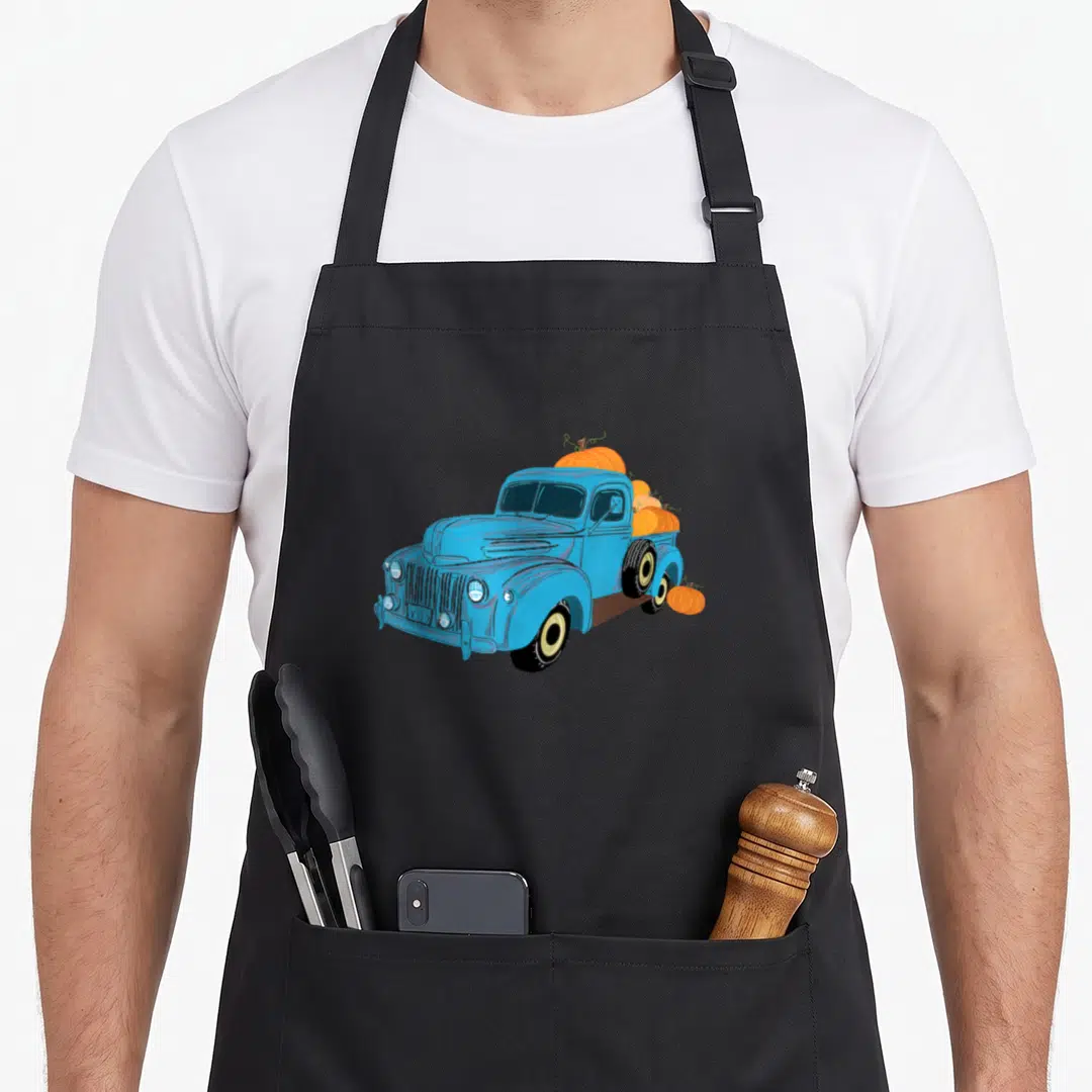 Fall truck apron - Blue cartoon truck with orange pumpkins in bed and one on ground — shown on a black cotton canvas apron against a white background