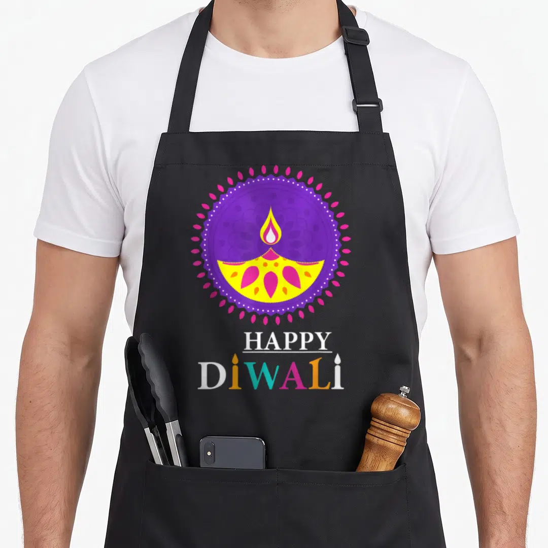 Festival diwali apron - Yellow and pink diya lamp inside purple mandala with HAPPY DiWALI text below — shown on a black cotton canvas apron against a white background