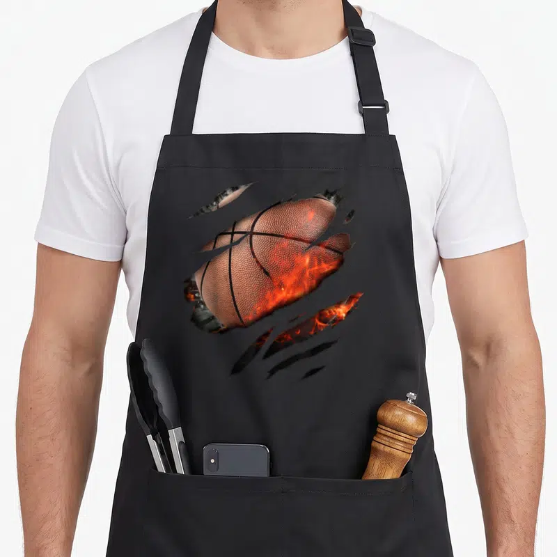 Basketballdesign basketball apron - Realistic orange basketball torn by diagonal claws with fire inside in brown — shown on a black cotton canvas apron against a white background