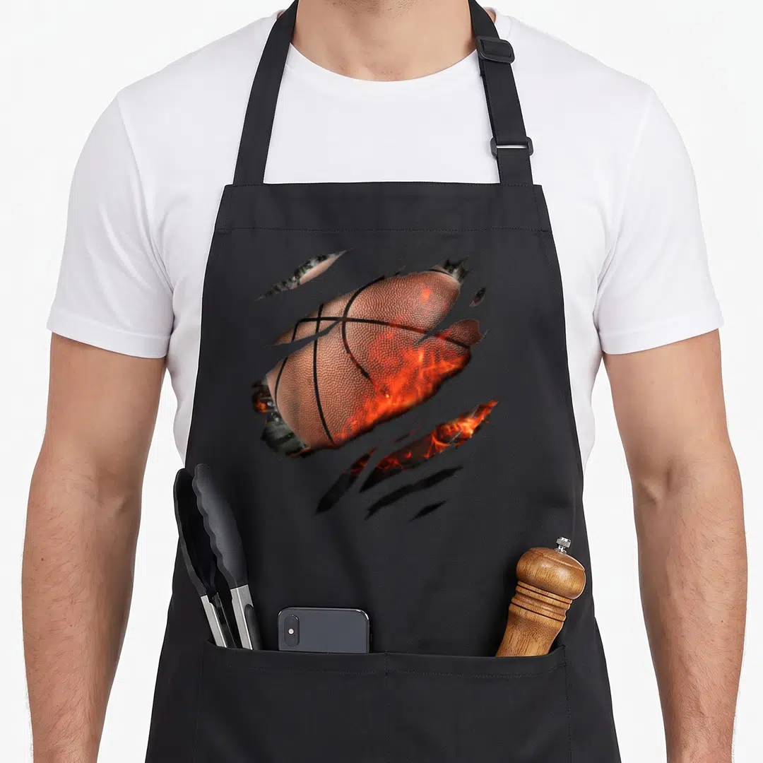 Basketballdesign basketball apron - Realistic orange basketball torn by diagonal claws with fire inside in brown — shown on a black cotton canvas apron against a white background
