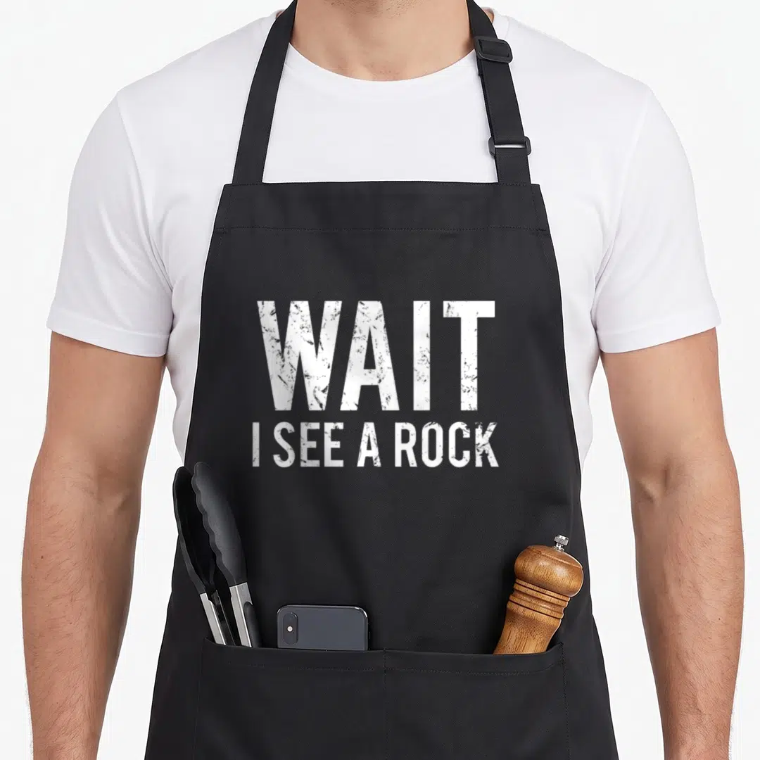 Geology minerals apron - White distressed text reading WAIT I SEE A ROCK stacked in two lines — shown on a black cotton canvas apron against a white background