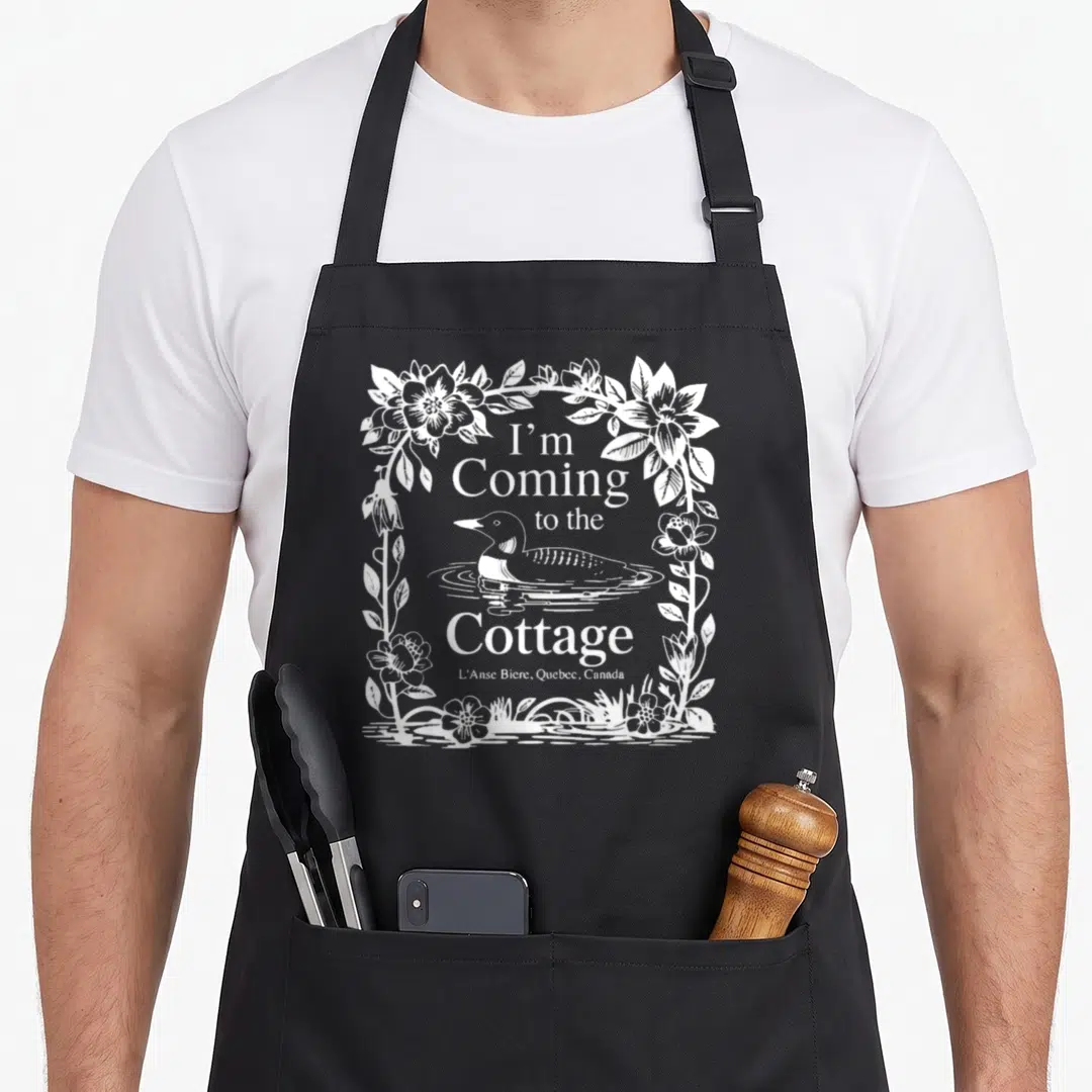 Come cottage apron - White line-art loon surrounded by floral border with I'm Coming to the Cottage text — shown on a black cotton canvas apron against a white background