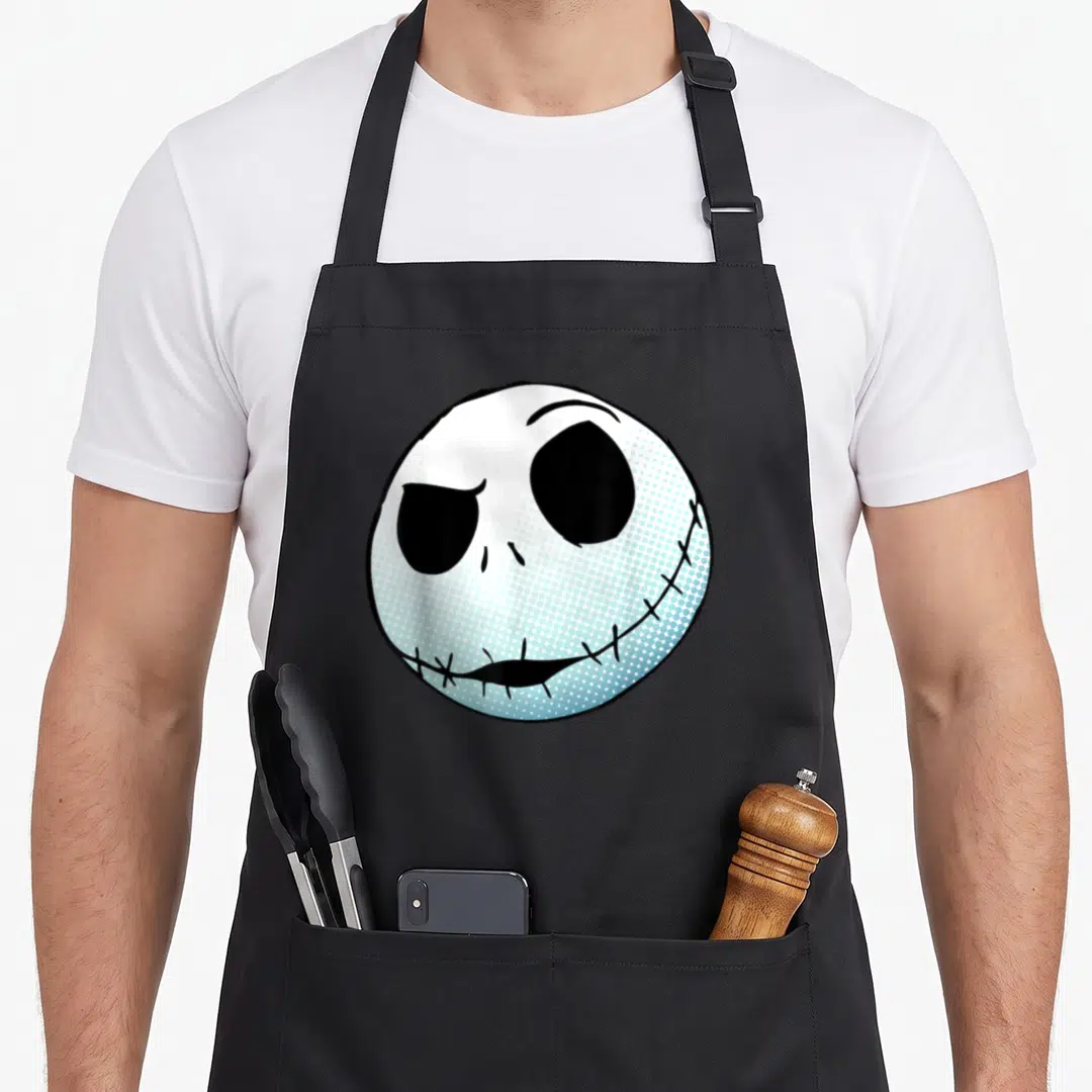 Cool christmas apron - Cartoon skeleton head in white light blue and black centered on fabric panel — shown on a black cotton canvas apron against a white background