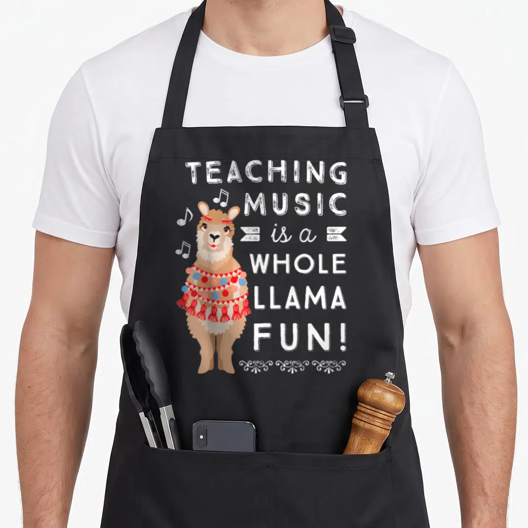Band music teacher apron - Cartoon llama with red and blue accessories next to stacked text TEACHING MUSIC is a WHOLE — shown on a black cotton canvas apron against a white background