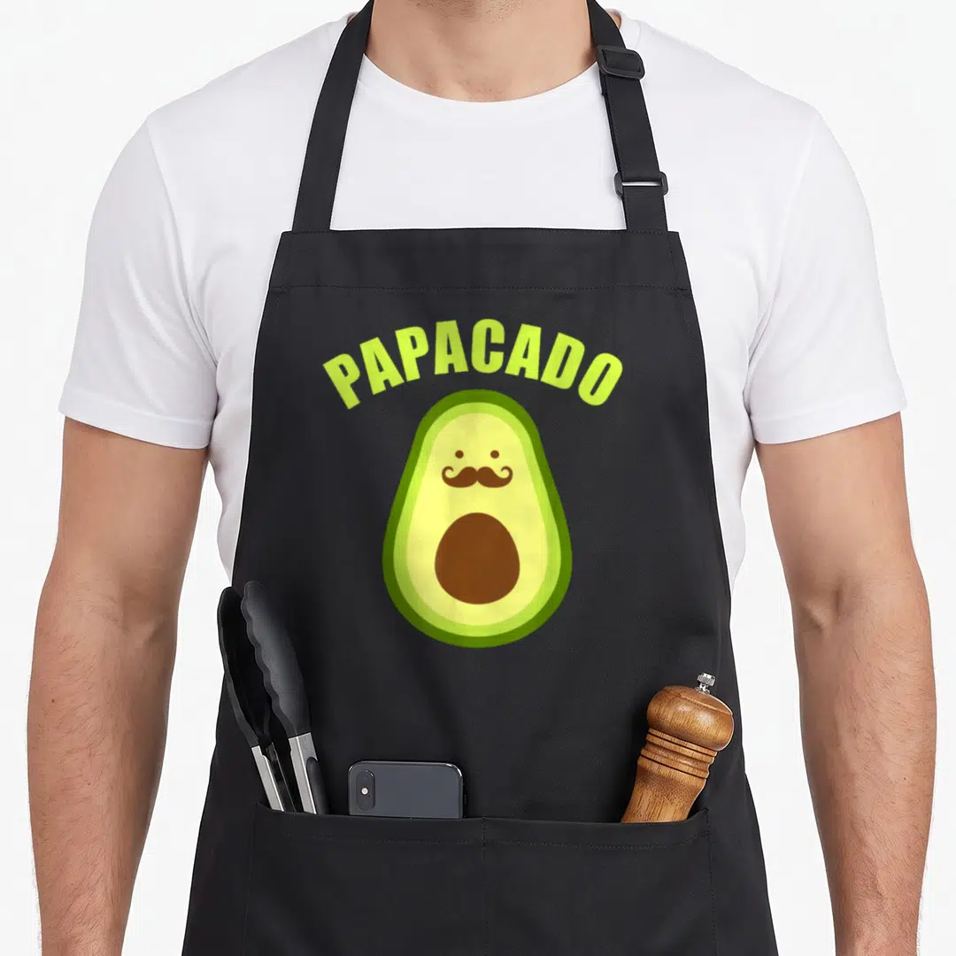 Papacado father day apron - Cartoon avocado with mustache and PIT under arched PAPACADO text in lime green — shown on a black cotton canvas apron against a white background
