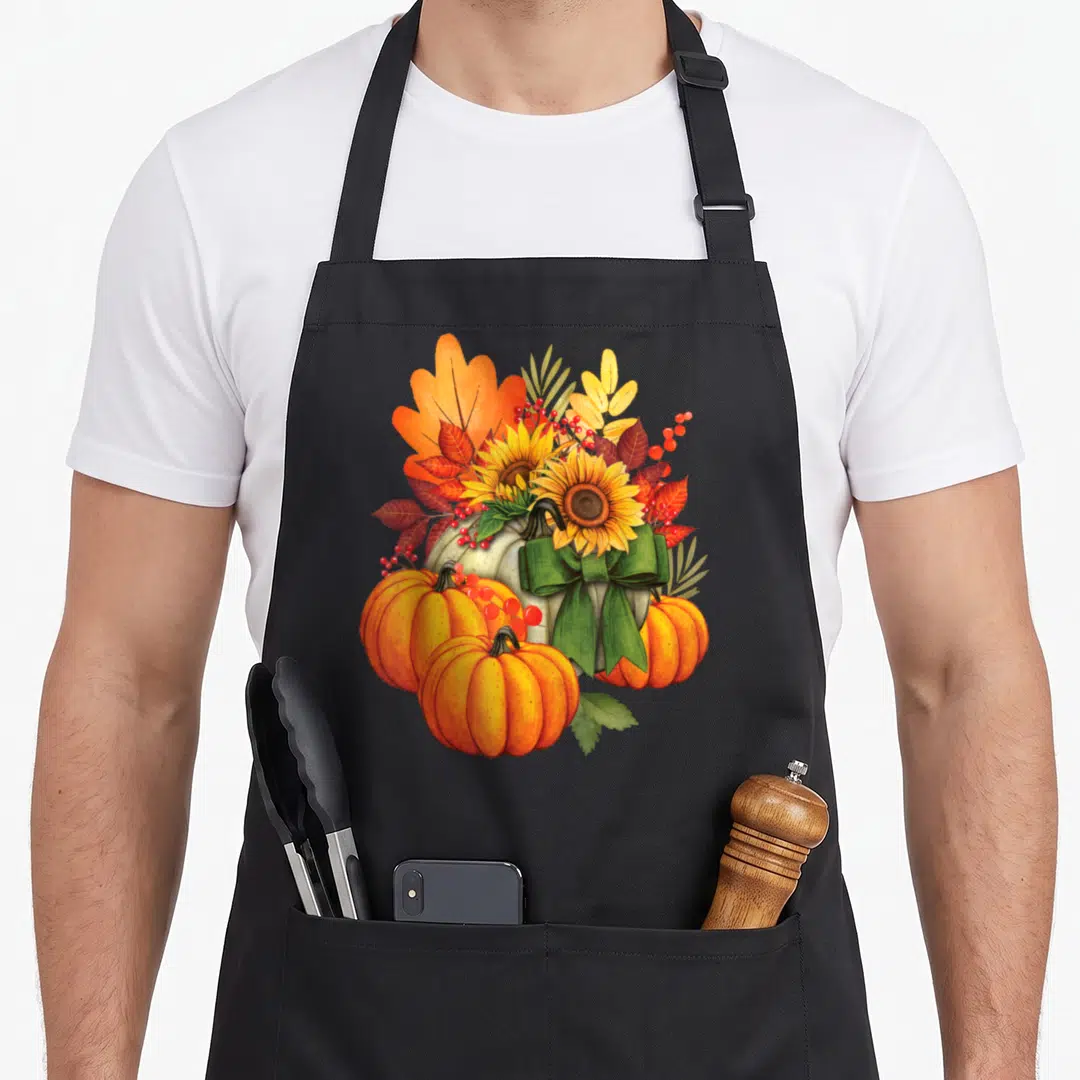 Holiday fall aprons - Watercolor cluster of orange pumpkins, yellow sunflowers, red leaves, and green ribbon bow — shown on a black cotton canvas apron against a white background