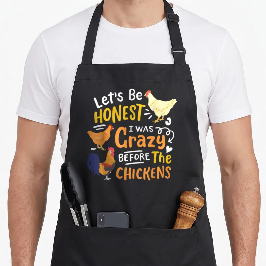 Funny honest chicken apron - Let's Be Honest I Was Crazy Before The Chickens text with three cartoon chickens — shown on a black cotton canvas apron against a white background