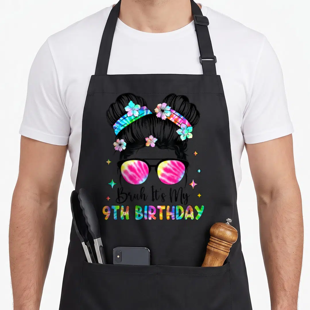 Funny bruh birthday apron - Cartoon girl with space buns and tie-dye sunglasses above 9th Birthday text — shown on a black cotton canvas apron against a white background