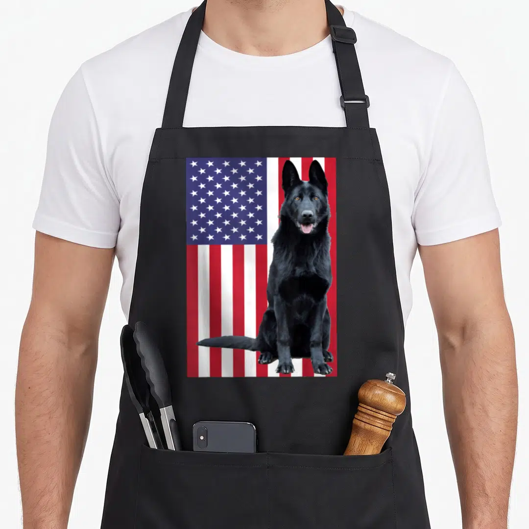 Cute shepherd german apron - Black German Shepherd dog sitting in front of American flag with red white and blue stripes — shown on a black cotton canvas apron against a white background