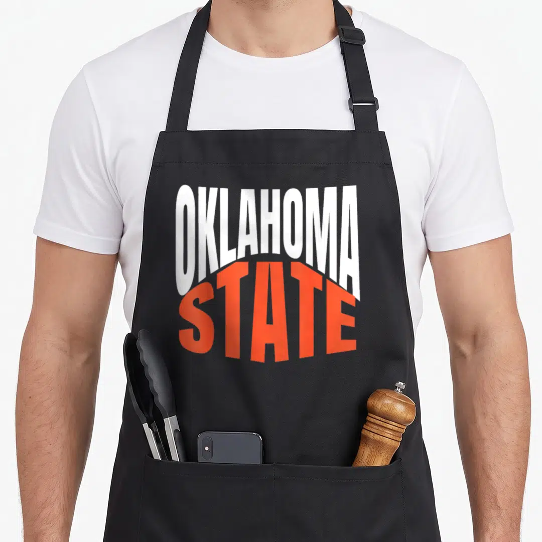 State oklahoma girl apron - White and orange typography reading OKLAHOMA STATE stacked vertically — shown on a black cotton canvas apron against a white background