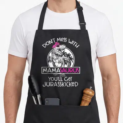 Youll mama apron - T-Rex with pink headscarf and text Don't Mess With Mamasaurus Youll Get Jurasskicked — shown on a black cotton canvas apron against a white background