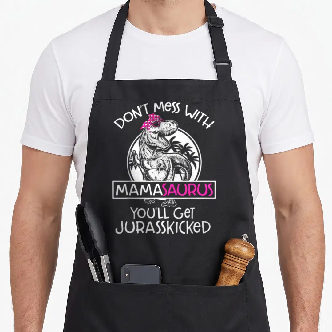 Youll mama apron - T-Rex with pink headscarf and text Don't Mess With Mamasaurus Youll Get Jurasskicked — shown on a black cotton canvas apron against a white background